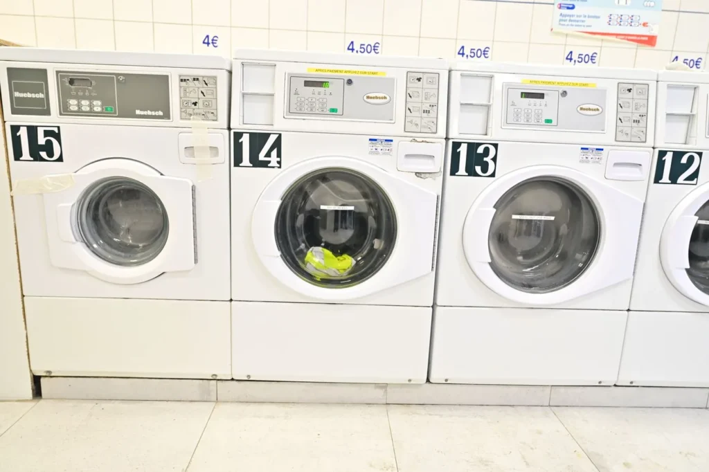 Lave-linges blancs numérotés 12 à 15, prix affichés au-dessus